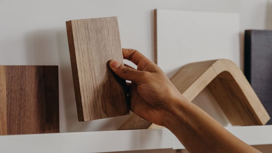 A hand takes a wood decor sample from a shelf among other board samples