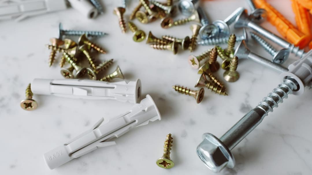 Wood screws, expansion wall plugs and a hex-head screw on a light worktop