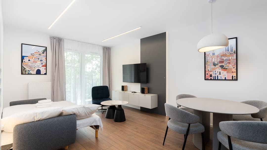 Light studio flat with a sofa bed opened out, a wall-hung TV unit under the television and a round table